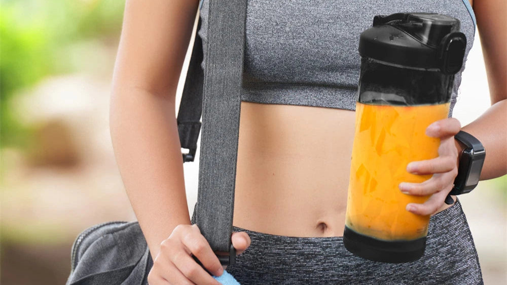 Person holding a blender with a smoothie, wearing a sports outfit outdoors.